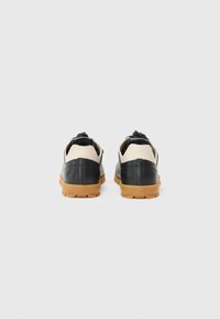 Scarpe in pelle nere e crema con una finitura texturizzata, suole in gomma naturale e distintivi anelli posteriori per il tiraggio. Design elegante con una forma arrotondata.