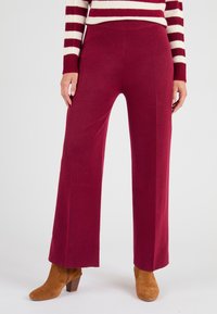 Pantalons larges bordeaux en tissu doux avec une taille élastique, associés à des bottines en daim marron, offrant une coupe décontractée.