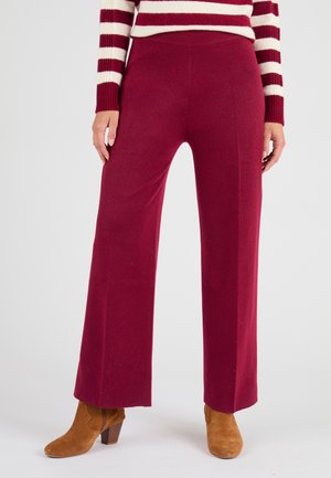 Pantalons larges bordeaux en tissu doux avec une taille élastique, associés à des bottines en daim marron, offrant une coupe décontractée.