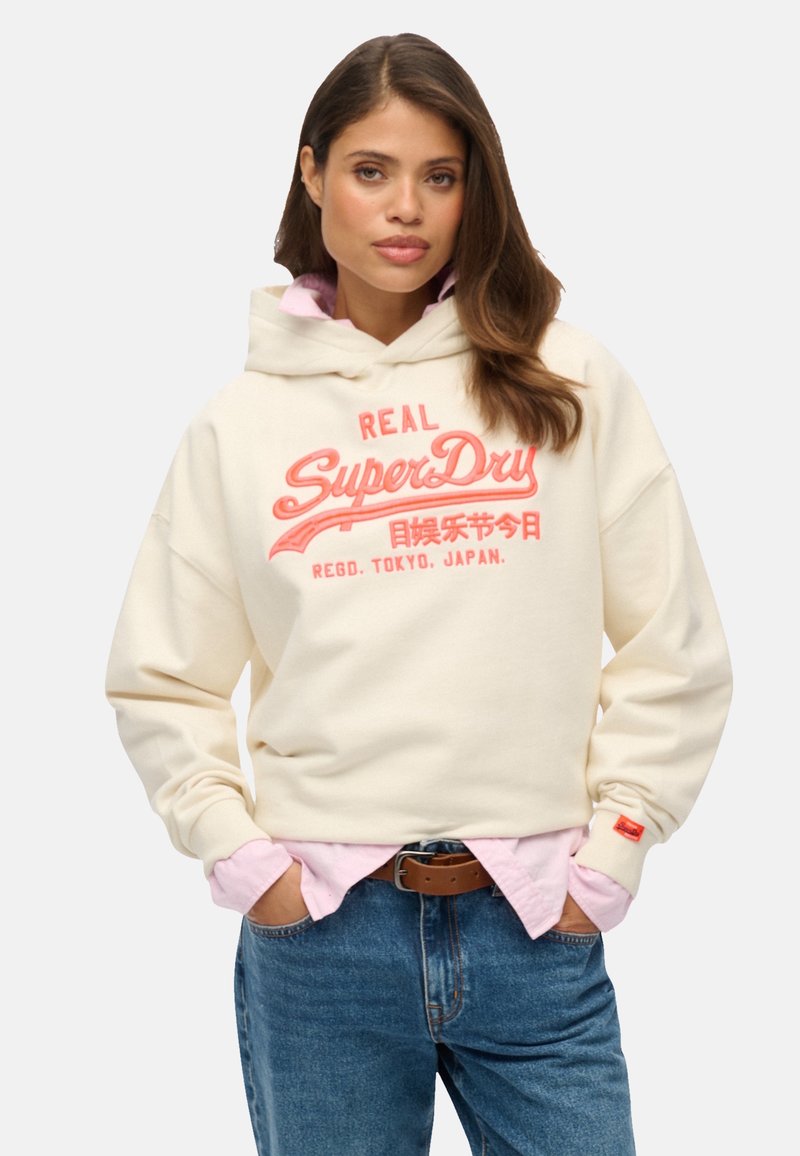 Crème hoodie met een rood en roze grafisch logo, voorzien van een capuchon met trekkoord, een relaxed fit en geribde manchetten. Gemaakt over een roze shirt.