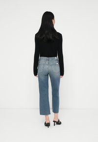 Jeans de ganga de cintura alta em azul claro, com corte reto, apresentando bolsos traseiros e desgastes mínimos. Combinados com uma blusa preta de manga longa.