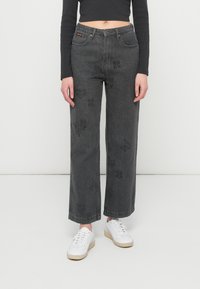 Φαρδιά, σκούρα γκρι τζιν με μπροστινές τσέπες και διακοσμητικά μαύρα μοτίβα από καρδιές και λουλούδια στα πόδια. Συνδυασμένα με λευκά αθλητικά παπούτσια.