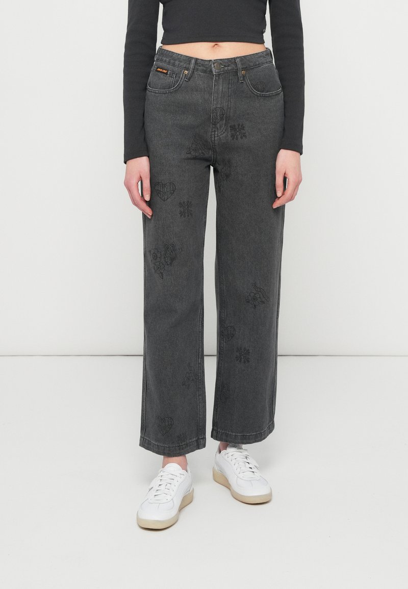 Φαρδιά, σκούρα γκρι τζιν με μπροστινές τσέπες και διακοσμητικά μαύρα μοτίβα από καρδιές και λουλούδια στα πόδια. Συνδυασμένα με λευκά αθλητικά παπούτσια.