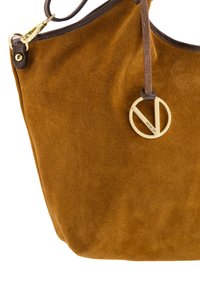 Braune Wildleder-Handtasche mit weicher Textur, die mit einem goldenen, kreisförmigen Logo-Akzent und einem dunklen Ledergriff versehen ist.