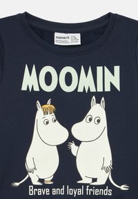Tumesinine puuvillane T-särk Moomini tegelastega, suurte "MOOMIN" tekstiga. Sile kangas, ümar kaelus ja lühikesed varrukad.