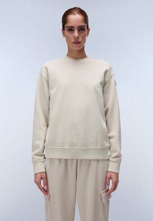 Beige sweatshirt met een ronde hals, ribbelboorden en een ribbelzoom. Beschikt over drop schouders en een gladde textuur. Gecombineerd met bijpassende beige broek.