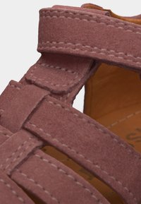 Κοντινό πλάνο των λουριών σανδαλιών από σουέντ σε σκόπινο ροζ χρώμα με ορατή ραφή και εσωτερική σόλα από ταμπά δέρμα.