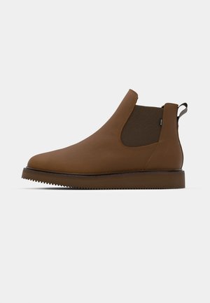 Stivale Chelsea in pelle marrone con pannelli laterali elasticizzati, punta arrotondata slim e suola in gomma testurizzata. Presenta un tab sul tallone.