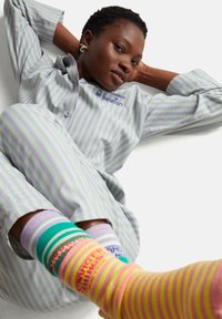 Conjunto de pijama a rayas en púrpura claro y verde con una camisa abotonada, combinado con calcetines coloridos y estampados con diversos diseños.