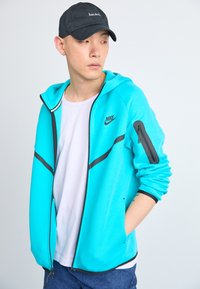 Nike tirkīza krāsa ar melnām akcentām, ar rāvējslēdzēju un rāvējslēdzēja kabatu uz piedurknes, apvieno ar baltu T-kreklu un džinsa šortiem. Kokvilnas maisījuma audums.