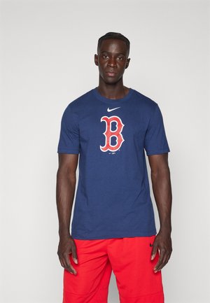 Camiseta de algodón color azul marino con un gran logo rojo y blanco de "B" en el frente y un logo de swoosh de Nike encima. El modelo lleva pantalones cortos rojos.