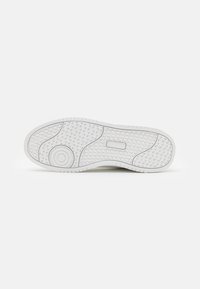 Weiße Sportschuhsohle mit strukturiertem Muster und kreisförmigem Detail, mit Rillen für Traktion und einem sauberen, minimalistischen Design.