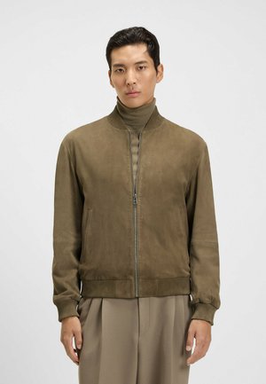 Olive green bomber jacket made of suede with a ribbed collar and cuffs, featuring a front zipper and side pockets. Smooth texture.