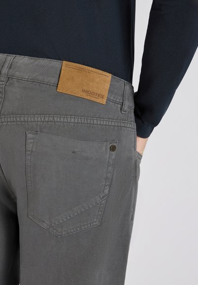Pantalones de algodón grises con una textura suave, que presentan un parche de cuero etiquetado con "INCOTEX" y detalles en el bolsillo trasero.