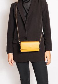 Borsa a tracolla in pelle gialla con forma rettangolare elegante, bordo nero a contrasto e tracolla in catena color oro.