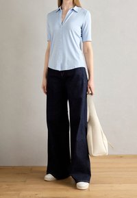 Camicia button-up azzurro chiaro a maniche corte abbinata a jeans a gamba larga blu scuro e sneakers bianche. L'outfit include una grande borsa tote bianca.