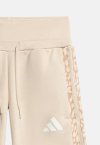 Μπεζ φόρμα με ελαστική μέση, κορδόνι, πλαϊνές τσέπες, ρίγα με λεοπάρ σχέδιο και λευκό λογότυπο Adidas στο αριστερό μηρό.