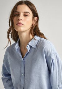 Camicia azzurro chiaro a maniche lunghe, realizzata in tessuto morbido e strutturato. Presenta un colletto classico, maniche lunghe e un logo ricamato discreto sul petto.
