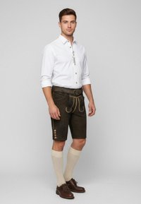 Traditionelle Lederhosen aus dunkelbraunem Wildleder mit gelben Akzenten, floralem Präge-Muster, einem passenden Gürtel und knielangen Socken.