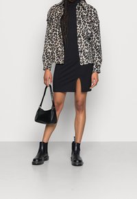 Kurtka dżinsowa w panterkę noszona na czarnej sukience z bocznym rozcięciem. Akcesoria to mała czarna torebka i czarne botki za kostkę.