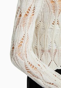 Gebreide trui in off-white met een ingewikkeld opengewerkt patroon. Heeft een gestructureerd ontwerp met lange mouwen, geometrische vormen en uitsparingen.