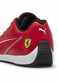 Basket rouge de sport avec un matériau synthétique lisse, un design épuré, des accents noirs, une semelle blanche et un logo Ferrari jaune sur le côté.