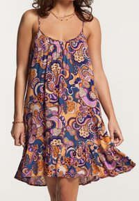 Robe d'été multicolore avec un motif floral et tourbillonnant. En tissu léger, elle présente des bretelles spaghetti et un ourlet à volants.