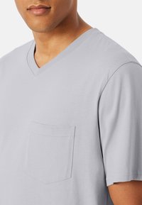 Man wearing a light gray V-neck T-shirt with a small chest pocket, shown from mid-chest to below the mouth.