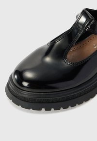 Sorte patent lær sko med rund tå, utskjæringsdesign og tykk svart gummisåle. Har subtil søm langs kantene.