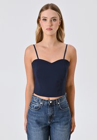 Top corto blu navy con sottili spalline a spaghetti e scollatura a cuore, abbinato a jeans di denim azzurri a vita alta.