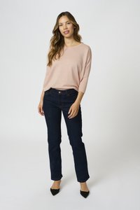 Svetlo roza pletena majica s širokim krojem, v kombinaciji s temno modrimi oprijetimi kavbojkami in črnimi čevlji s koničastim nosom. Preprost in moden dizajn.