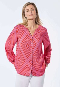 Rode en roze blouse met lange mouwen en een geometrisch ruitpatroon, knoopsluiting aan de voorkant en een v-hals ontwerp. Gemaakt van lichtgewicht stof.