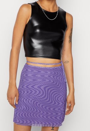 Femme portant un crop top noir sans manches en cuir synthétique et une mini-jupe à motif tourbillon violet avec des bretelles enveloppantes.