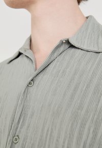 Camicetta verde chiaro con colletto, realizzata in tessuto a costine; presenta due piccoli bottoni e un neckline curvo.