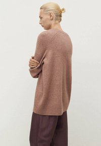 Loose-fitting, rose-colored knit sweater with a ribbed hem and sleeves, made of soft material; worn with dark, wide-leg trousers.