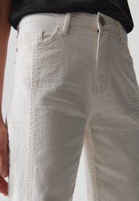 Jeans beige chiaro in denim con una finitura testurizzata, caratterizzati da un classico design a cinque tasche e una chiusura a bottone in vita.