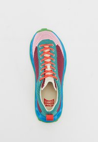 Sapatilha multicolorida com um upper tricotado em azul, rosa e burgundy, apresentando atacadores vermelhos, uma sola verde, e um design texturizado e flexível.