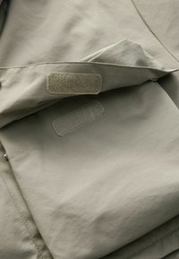 Tăblă de material de un verde oliv deschis, cu o textură netedă, având petice cu Velcro și un design curat al cusăturilor.