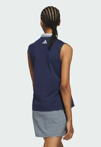 Navy sleeveless top with a white collar, featuring a small logo on the back. Paired with a checkered skirt in blue and white.
