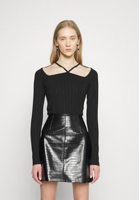 Top preto de manga longa com textura canelada e decote cruzado, combinado com uma saia alta em pele sintética de crocodilo preta.