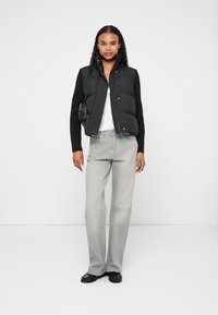 Melnā pūkainā veste ar slāni virs melna ribota džempera, balta T-kreklu un gaiši pelēkam biksēm; papildināta ar melnām kurpēm un mazu somiņu.