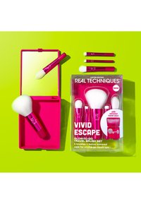 Cinq pinceaux de maquillage d'un rose vif et un étui de voyage avec miroir sur un fond vert citron, étiquetés "Real Techniques Vivid Escape".