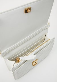 White quilted handbag with gold hardware and a zippered pocket. Interior features multiple card slots and a smooth lining.