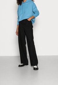 Felpa blu con cappuccio, vestibilità comoda, abbinata a jeans neri a gamba larga. Scarpe nere con un accento bianco. Colori solidi, design casual.