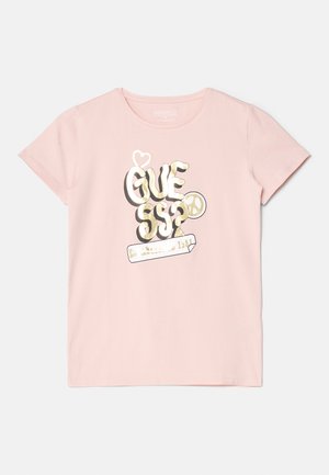 Lyserød kortærmet skjorte med metallisk gyldent stiliseret "GUESS"-tekst, et hjerte, fredssymbol og en skitseret rektangeldesign foran.