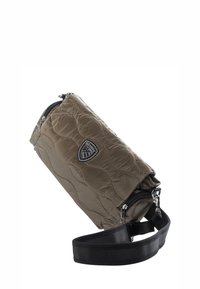 Gesteppte olivgrüne Taillentasche mit schwarzem verstellbarem Riemen, silbernem Reißverschluss und einem kleinen schwarz-weißen Emblem auf der Vorderseite.