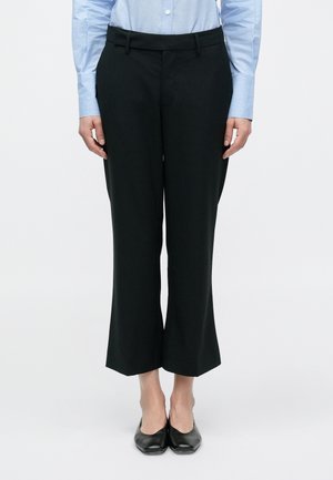 Pantalon évasé noir à texture lisse, avec une large ceinture et une coupe ajustée. Porté avec une chemise cintrée bleu clair.