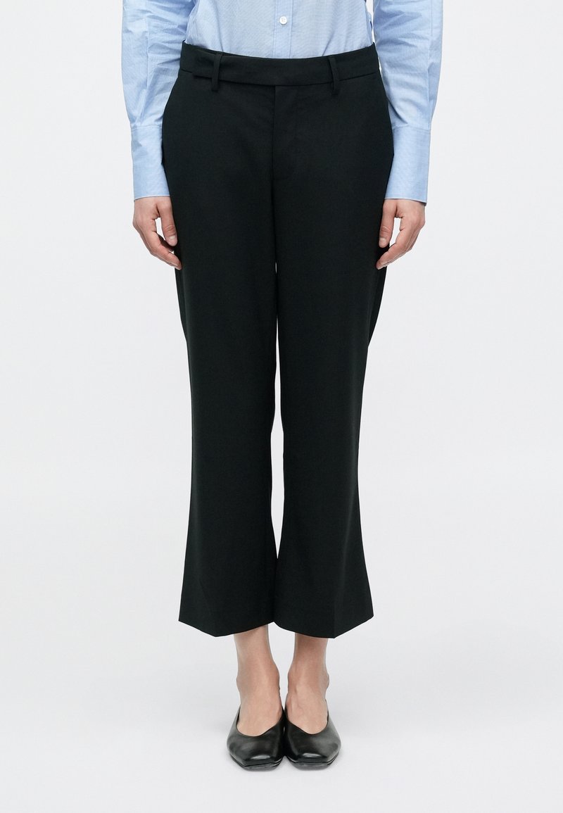 Μαύρο παντελόνι καμπάνα με λεία υφή, διαθέτει φαρδιά μέση και εφαρμοστή γραμμή. Φοράει με ανοιχτό μπλε εφαρμοστό πουκάμισο.