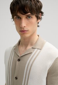 Lightweight short-sleeve shirt in beige and white, featuring a collar, button front, and textured stripes along the shoulders.