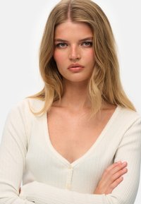 Ribbet cremede cardigan med dyb V-udskæring, lange ærmer og små runde knapper, der har et struktureret stof og en delikat scalloped kant.